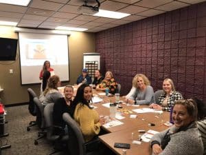 A group of people in a meeting. A woman si giving a presentation on the projector screen.